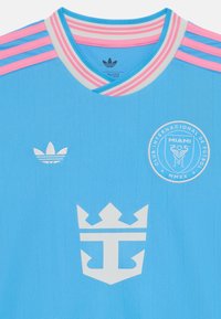 Camiseta de fútbol azul claro con rayas verticales, un cuello a rayas en rosa y gris, y los logotipos de Adidas y del equipo en blanco.