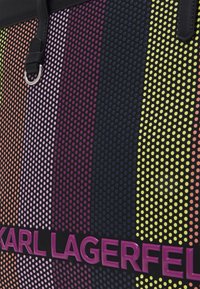 Bolso texturizado con un degradado de patrones de puntos en colores: naranja, rosa, púrpura, azul y amarillo. Presenta un detalle del logo en púrpura.