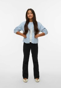 Šviesiai mėlynas megztinis su apvaliais mygtukais, dėvimas ant balto viršaus, derinamas su juodomis išplatintomis kelnėmis ir kreminės spalvos slip-on avalyne.