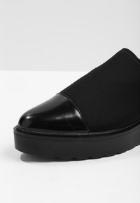 Černá bota s hladkým koženým špičkou a textilním svrškem, vybavená silnou gumovou podešví a bezproblémovým designem. Matný povrch po celé ploše.