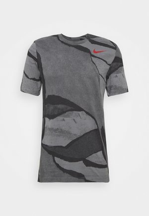 Szara koszulka z abstrakcyjnymi czarnymi i szarymi wzorami, krótkie rękawy, okrągły dekolt oraz czerwone logo Nike blisko ramienia.
