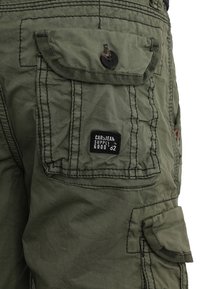 Pantaloni cargo verdi realizzati in tessuto con finitura testurizzata. Presentano più tasche, una chiusura con bottone e un'etichetta con logo sul lato.