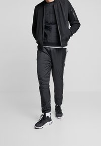 Svart träningsoverall med en bomberjacka med meshärmar, en vadderad topp och slimmade joggerbyxor, i kombination med svart och vita sneakers.