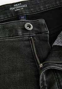 Jeans negri din denim, slim fit, cu fermoar și accesorii din argint, având o finisare texturată. Eticheta indică "NEXT PERFORMANCE" și mărimea "34R."