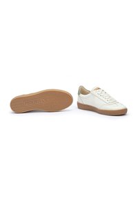 Baskets en cuir blanc avec une semelle en caoutchouc texturée, présentant une finition lisse, des lacets et un accent vert au niveau du talon. Logo de la marque sur la semelle.