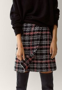 Wollen blend rok met een zwart-wit-rode ruitpatroon, een wikkelontwerp en een getailleerde snit. Gecombineerd met kniehoge zwarte laarzen.