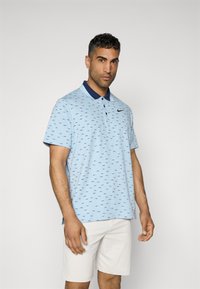 Light blue polo shirt with navy collar, featuring a subtle all-over pattern. Short sleeves, button placket, and Nike logo on the chest.
