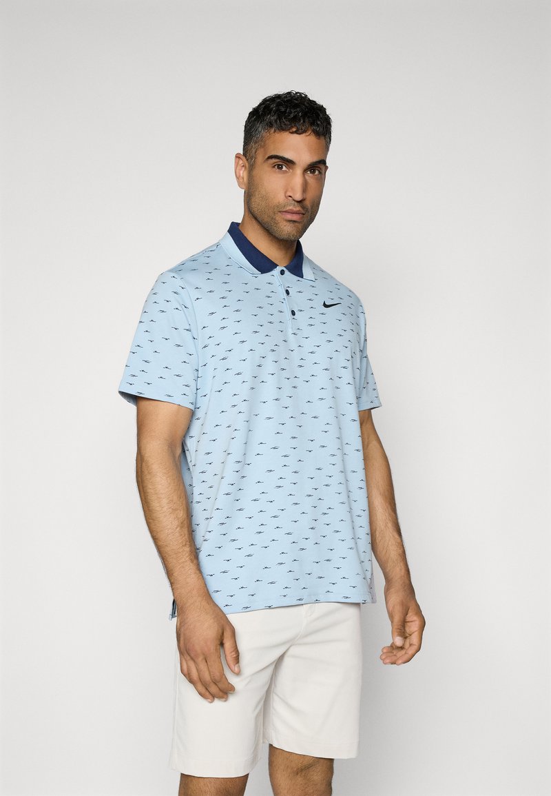 Light blue polo shirt with navy collar, featuring a subtle all-over pattern. Short sleeves, button placket, and Nike logo on the chest.