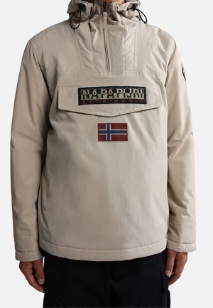 Beige hættejakke med frontklap, lynlås, Napapijri-logo og norsk flagpatch båret af en person med armene ned langs siden.
