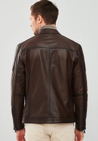 Brown leather jacket with a textured finish, features a high collar and zippers on the sleeves, showcasing a fitted design.