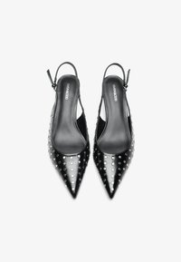 Décolleté nere con cinturino a slingback, punta affilata, realizzate in materiale lucido e decorate con borchie argentate disposte in un motivo a pois sulla superficie.