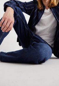 Vaqueros de denim en azul oscuro con una textura suave y corte recto, combinados con una camiseta blanca y una camisa a rayas en azul marino.