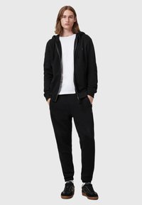 Black zip-up hoodie over a white t-shirt, paired with black sweatpants and black sneakers. Features a relaxed fit and soft texture.