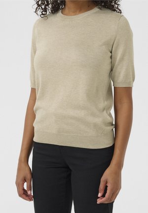 Beżowy sweter z krótkim rękawem i okrągłym dekoltem, z ribbowanym dołem, wykonany z miękkiego materiału, noszony z czarnymi spodniami, prezentujący gładką teksturę.