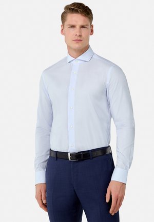 Camicia a righe blu chiaro con colletto button-down, maniche lunghe e una cintura nera. Indossata con pantaloni navy, caratterizzati da una finitura testurizzata.