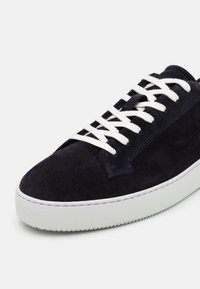 Marinblå mockasinöjd med vita snören, strukturerad yta och en tjock vit gummisula med en subtil mönstrad slitbana.