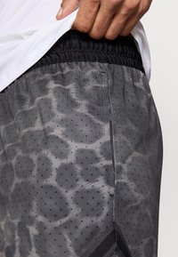 Γκρι αθλητικό σορτς με υφασμάτινο μοτίβο και μαύρες λεπτομέρειες, ελαστική μέση και μικρές οπές για αερισμό.