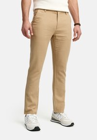 Chinos beige de algodón, con corte ajustado, parte delantera plana y bolsillos laterales, combinados con zapatillas deportivas blancas y grises.