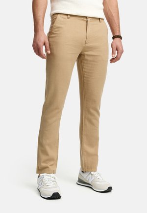 Beige chinos made of cotton, featuring a slim fit, flat front, and side pockets, paired with white and gray athletic shoes.