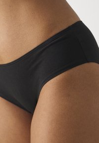 Black cotton brief with a smooth texture, seamless edges, and a mid-rise design. Focus on fit around the waist and thigh.