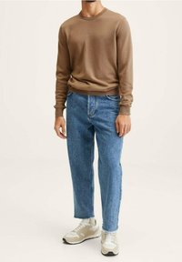 Maglione lungo marrone a maniche lunghe, jeans azzurri a vestibilità comoda e scarpe sportive beige. L'outfit presenta un design semplice e una leggera consistenza.