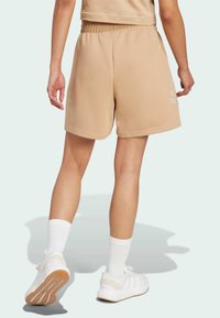 Pantalones cortos deportivos en color beige con una cinturilla elástica, un ajuste relajado y tres rayas horizontales en un tono más claro en el lado izquierdo.