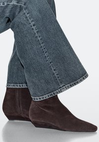 Braune Wildleder-Stiefeletten mit spitzer Zehenpartie und Keilabsatz, kombiniert mit weiten Denim-Jeans mit rohem Saum.