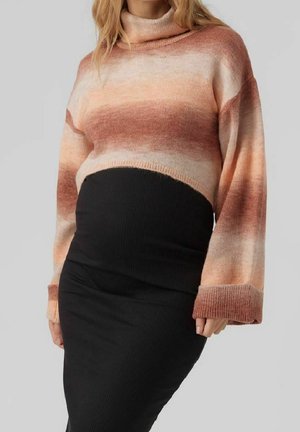 Femme portant un pull à col roulé rayé rose et marron et une jupe noire ajustée sur un fond gris.