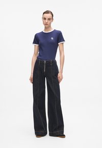 Marineblauwe geribbelde t-shirt met witte manchetten en een klein logo, gecombineerd met high-waisted donkere denim wijde broek met contrasterende stiksels.