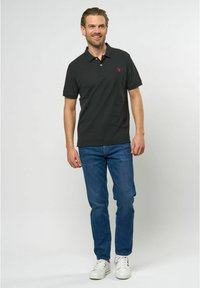 Tmavo šedý polo tričko s golierom a krátkymi rukávmi, s malým červeným logom. Nosí sa s modrými džínsami a bielymi teniskami.