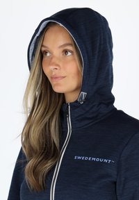 Felpa con zip di colore blu navy, dotata di zip anteriore, cappuccio foderato e dettagli con logo. Caratterizzata da un tessuto testurizzato e un design elegante.