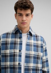 Blauw-wit geruite flanellen overhemd met een spreidkraag, knoopsluiting aan de voorkant en twee borstzakken. Zachte textuur, casual ontwerp.