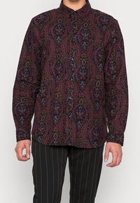 Long-sleeve button-up shirt in dark fabric featuring a paisley pattern in red, purple, and green hues. Black buttons and adjustable cuffs.