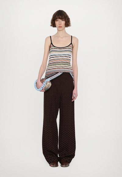 Multicolor striped tank top with black trim, paired with wide brown zigzag-patterned pants. Model holds a round purse with light blue chain.