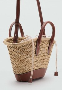 Sac en paille tissé avec des accents en cuir marron, doté de deux poignées, d'une fermeture à cordon et d'un fond arrondi.