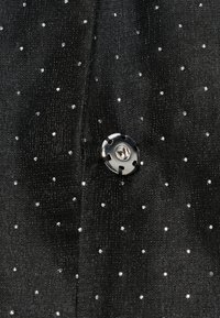 Čierna tkanina s texturovaným povrchom a striebornými kovovými bodkami. Výrazne je zobrazený okrúhly strieborný gombík so štyrmi otvormi.