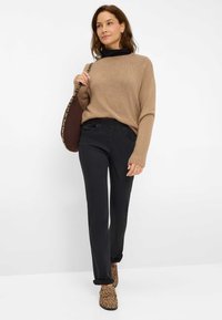 Brauner Strickpullover, schwarze Hose und braune Ankle-Boots mit Leopardenmuster. Das Modell trägt eine braune Tasche mit einem Leopardenmuster-Gurt.