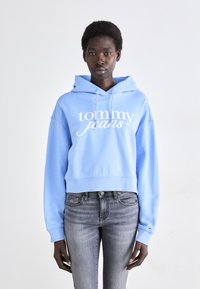 Haut cropped bleu clair avec le texte blanc "tommy jeans", cordons de serrage et ourlet côtelé. Associé à un jean skinny gris. Design simple.