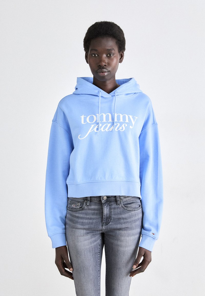 Haut cropped bleu clair avec le texte blanc "tommy jeans", cordons de serrage et ourlet côtelé. Associé à un jean skinny gris. Design simple.