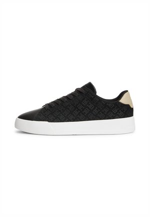 Sneaker nera low-top con motivo monogramma, lacci neri, suola spessa bianca e linguetta beige sul tallone, mostrata di profilo su sfondo bianco.