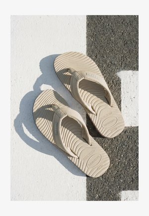 Infradito Havaianas beige con suole testurizzate posate su una superficie di pavimentazione a strisce bianche e nere alla luce del sole.