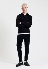 Zwarte lange mouwen polo met kraag, slim fit. Gecombineerd met donkergroene fluweelbroek en zwarte instappers. Witte onderhemd zichtbaar.