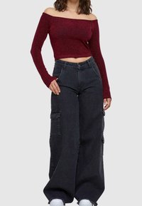 Burgundy off-the-shoulder lyhyt toppi pitkillä hihoilla, yhdistettynä korkeavyötäröisiin mustiin leveälahkeisiin cargo-housuihin, joissa on taskuja.