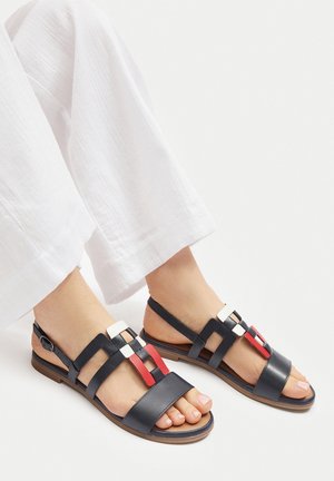 Skórzane granatowe sandały na płaskiej podeszwie. Posiadają wielokolorowe geometryczne akcenty w kolorach czerwonym, białym i czarnym na górnych paskach.