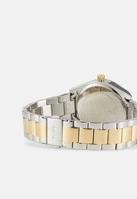 Silver and gold-tone watch featuring a stainless steel bracelet with alternating links, round case, and a gold crown on the side.
