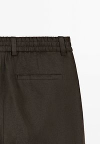 Close-up of black pants waistband with elastic and belt loops, featuring a single back welt pocket on the right side.