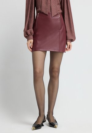 Korte bordeauxrode faux leren rok met twee ritszakken, gecombineerd met sheer zwarte panty's en zwarte slingback schoenen met gouden accenten.