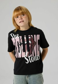 Svart bomulls-T-skjorte med rosa og hvit tekst, "The Rolling Stones," og en glitrende lepsemotiv. Kortermet med rund hals.