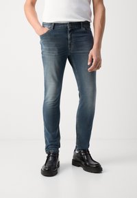 Sötétkék, slim fit farmernadrág, elhalványult részletekkel, öt zsebes kialakítással, fekete bokacsizmával párosítva.