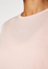 Lyserød bomulds T-shirt med rund halsudskæring. Har et lille, blåt broderet Puma-logo på brystet. Glat tekstur.